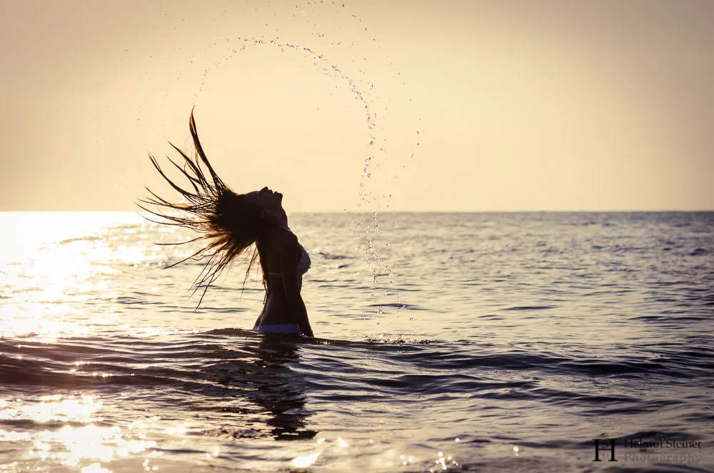 Girl standing in the sea swinging hair during sunrise
