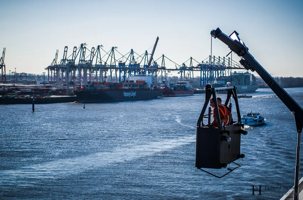 Two men in a window cleaning elevator looking over the harbour of Hamburg