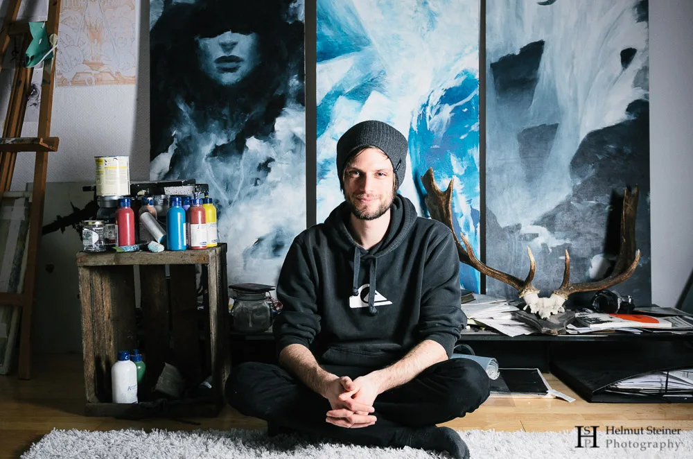 Portrait of a young artist sitting in front of his paintings