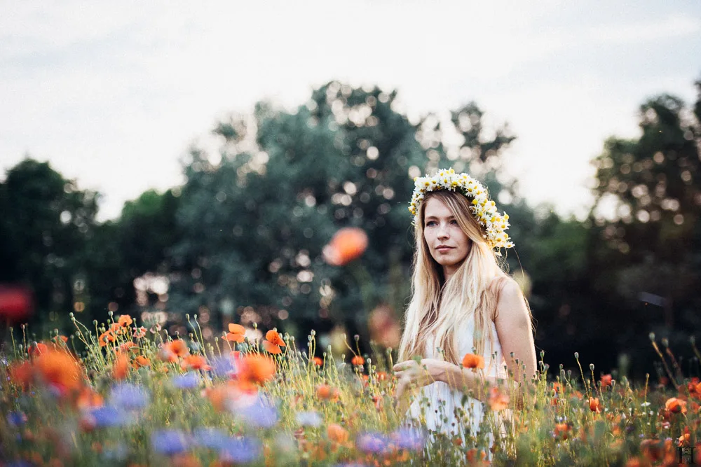 Portrait of a girl standing in a wild poppies field with a girdle of chamomile flowers