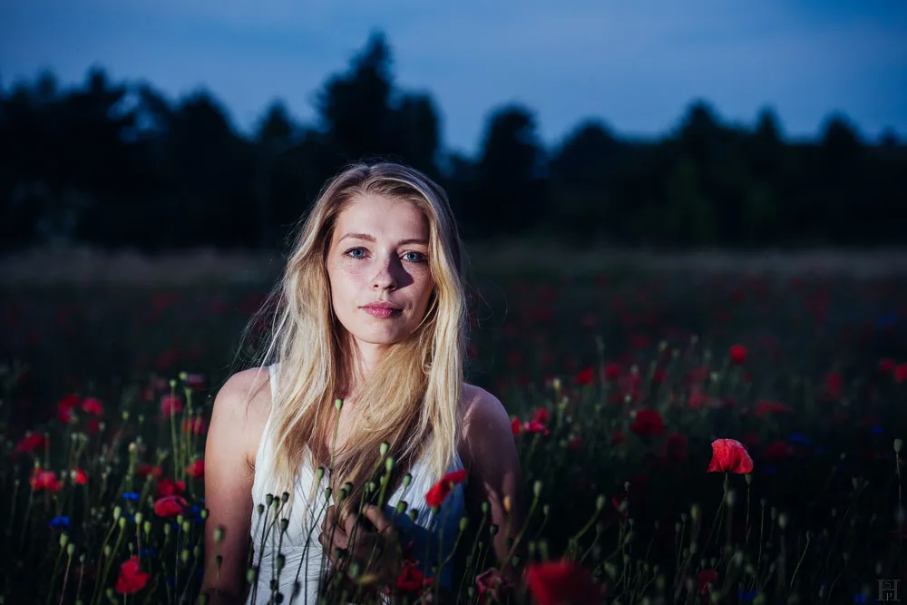 Portrait of a girl standing in a wild poppies field with a white summer dress