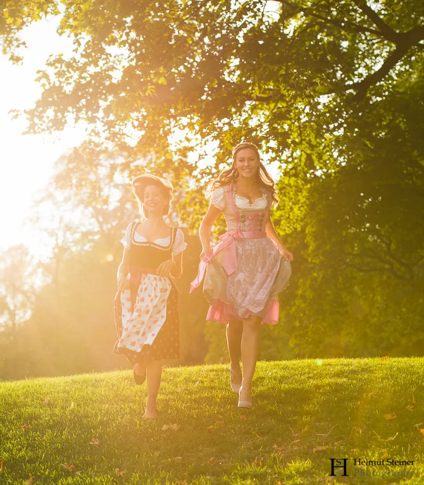 Girls in traditional German/Austrian dresses (called Dirndl) running down a hill with the sun setting behind them.