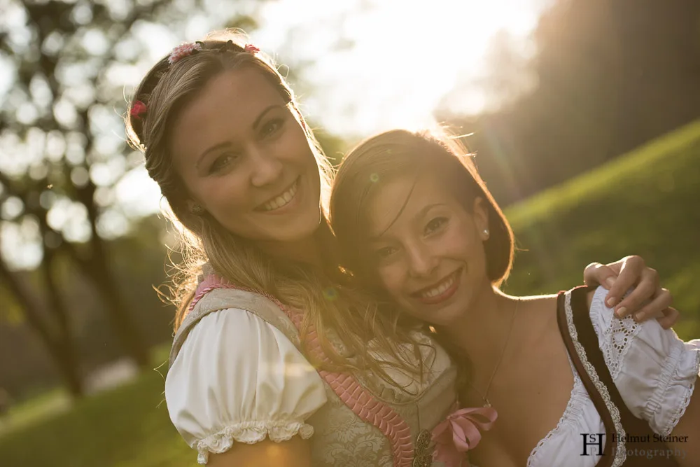 Portrait of two girls in traditional German/Austrian dresses (called Dirndl) with the sun setting behind them.