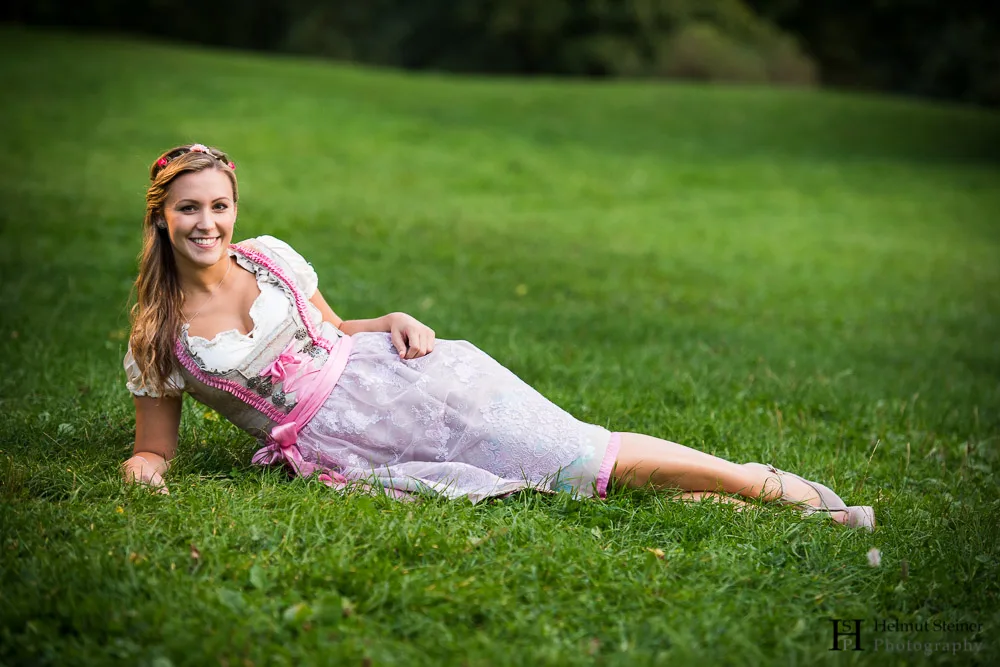A blond young girl in a traditional German/Austrian dress (called Dirndl) lying in the grass.